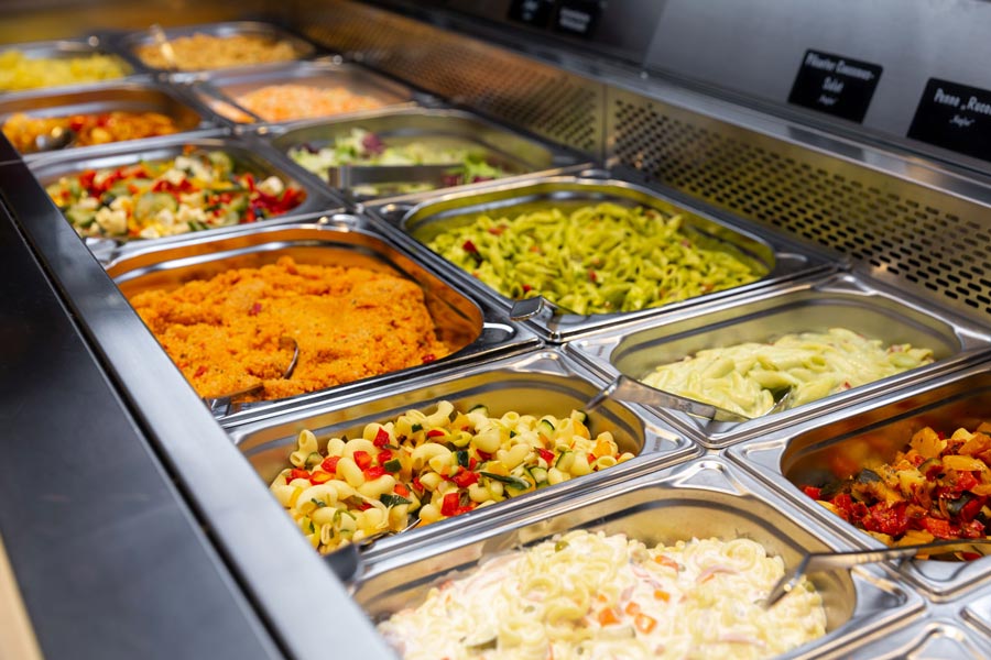 Vielfältige Salatbar mit verschiedenen Nudel- und Gemüsesalaten in Edelstahlbehältern.
