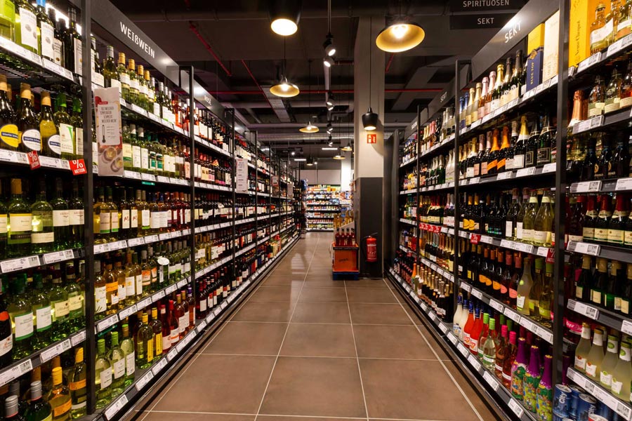 Getränkeabteilung mit langen Regalen voller Wein und Spirituosen im Supermarktgang.