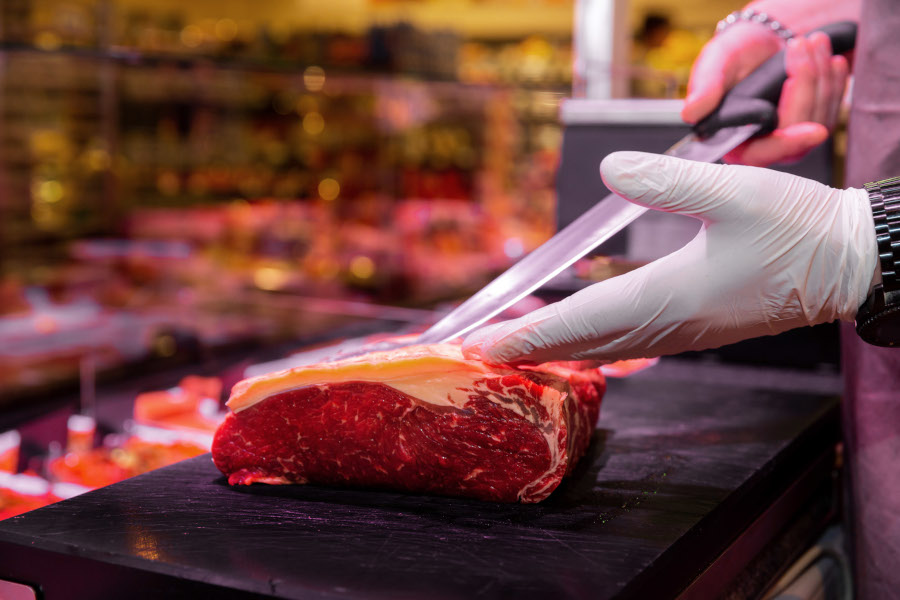 Metzger schneidet ein großes Stück Rindfleisch an der Frischetheke.